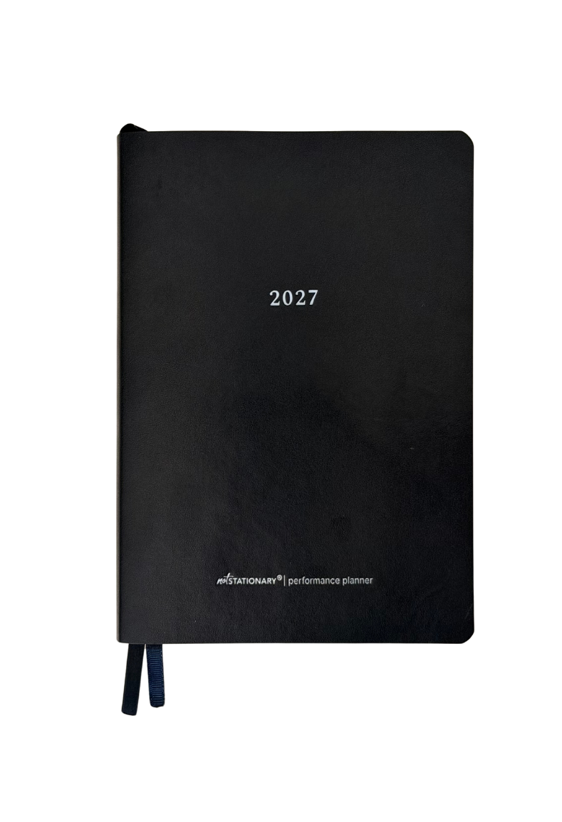 A black hardcover 2027 performance planner with white text and two dark blue ribbon bookmarks, shown on a plain white background.