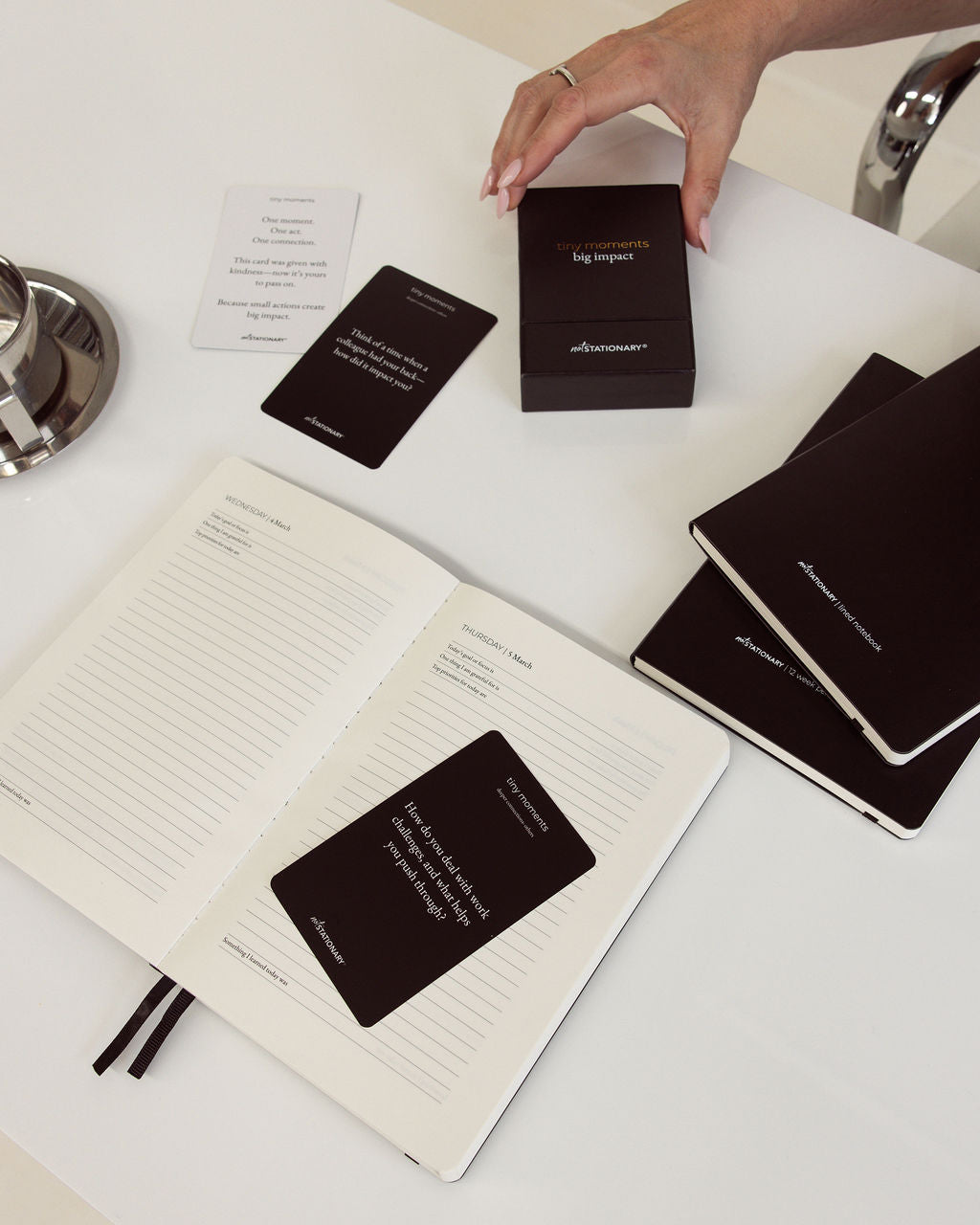 Person interacting with black diary and planner and cards on a white surface