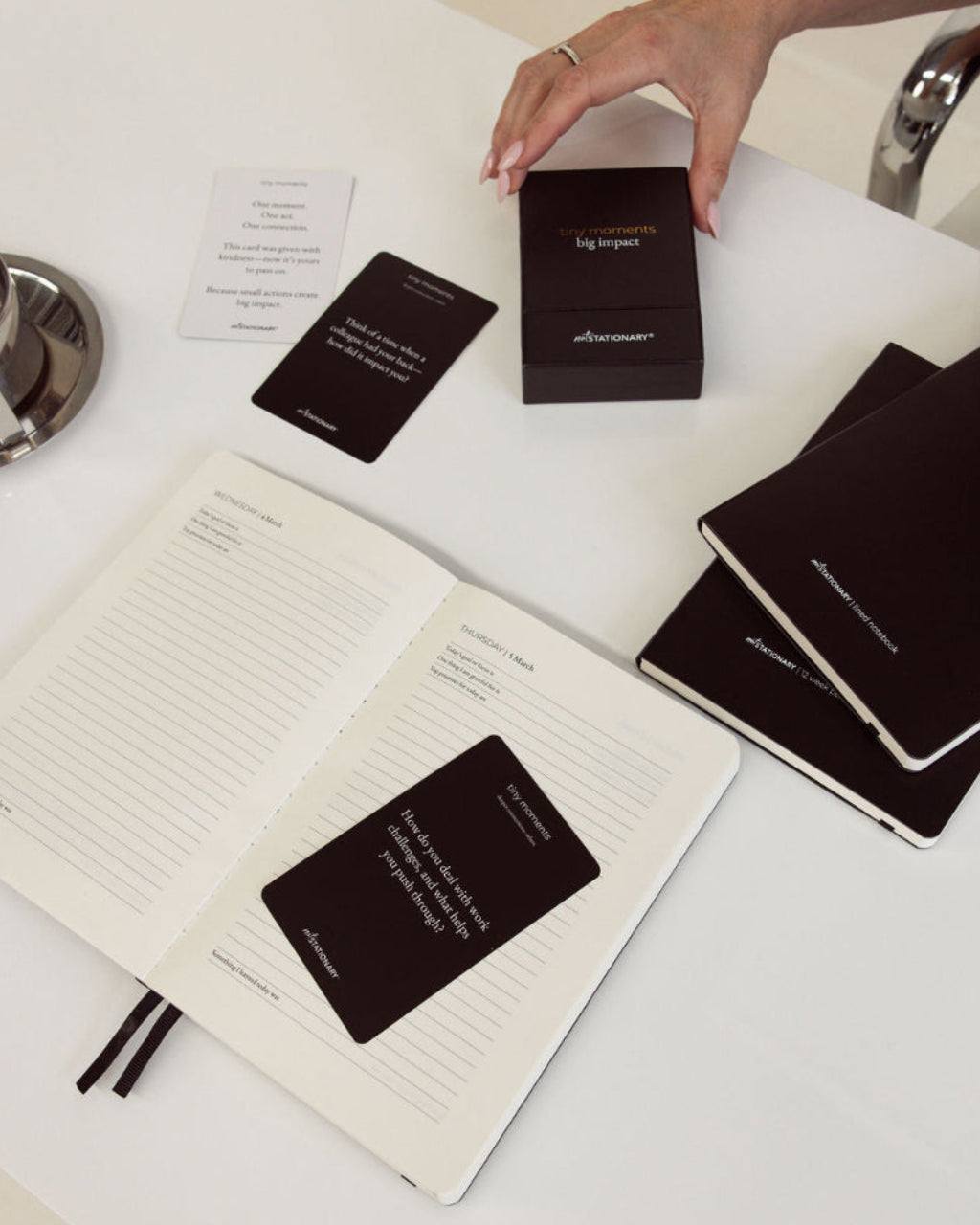 Person interacting with black diary and planner and cards on a white surface