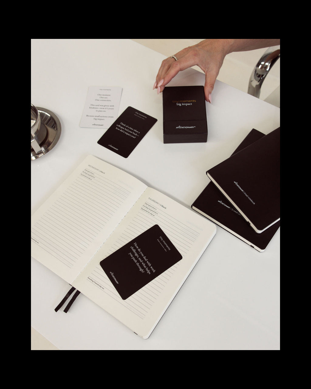 Person interacting with black diary and planner and cards on a white surface