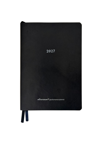 A black hardcover 2027 performance planner with white text and two dark blue ribbon bookmarks, shown on a plain white background.