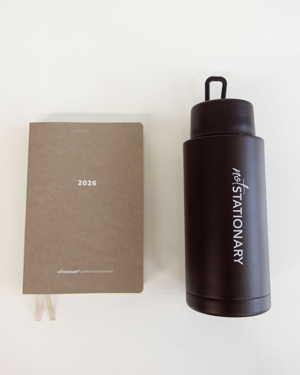 Brown notebook and black water bottle with '2026' and 'STATIONARY' text on a white background