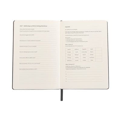 An open hardcover journal showing two interior pages with printed reflection prompts and a values chart, photographed on a plain white background.