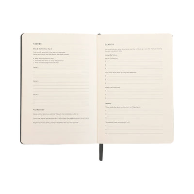 An open notebook showing two cream-colored interior pages with printed reflection prompts under headings 'VALUES' and 'CLARITY', photographed on a plain white background.