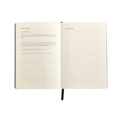 An open hardcover notebook showing two cream-colored lined pages with the heading 'GOALS 2037' and black text, held open by a black ribbon bookmark against a white background.
